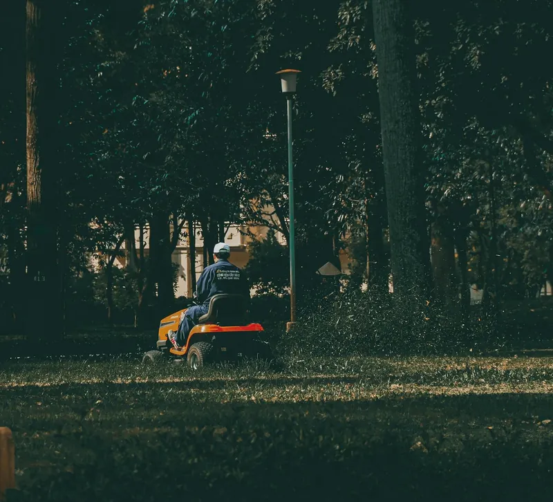 Lawn-care professional operating a ride-on mower in a green park